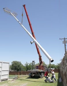 Three workers put all their weight into steadying a light pole as it comes down at Bronco Stadium Monday afternoon. The 40-year-old home-mamufactured lights are being relocated to the Clarendon softball field in preparation for the installation of new modern lights at the football field. Enterprise Photo / Roger & Ben Estlack