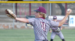 Baseball pitcher in a gray pinstripe uniform and maroon cap winds up to throw on the field, ball in his raised right hand.