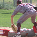 A baseball runner slides into a base while a fielder reaches to tag him, both players in gray uniforms on a dirt infield.