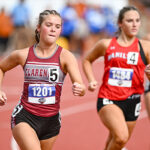 Female sprinters racing on a red track; lead runner in maroon top with bib 1201.